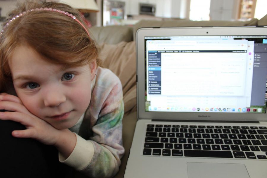 Journalism and English teacher Mandy Krause attempts to teach her classes while her three year-old, Rory, who would normally be in preschool everyday, hangs on her for attention.  Now that schools are closed, this is the dilema of many families with parents who normally work full-time, especially with children too young to have their own e-learning to work on.