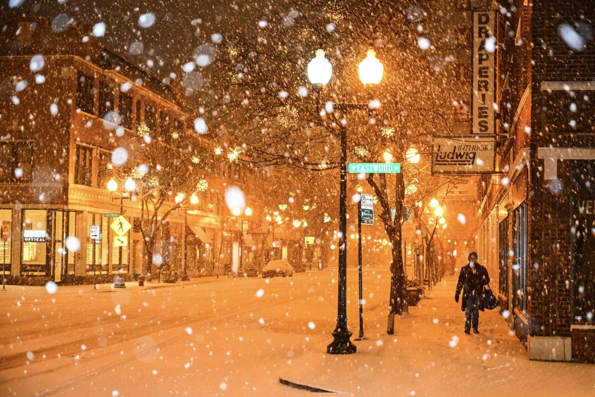 A woman walks down the sidewalk in Lincoln Square during snowfall.